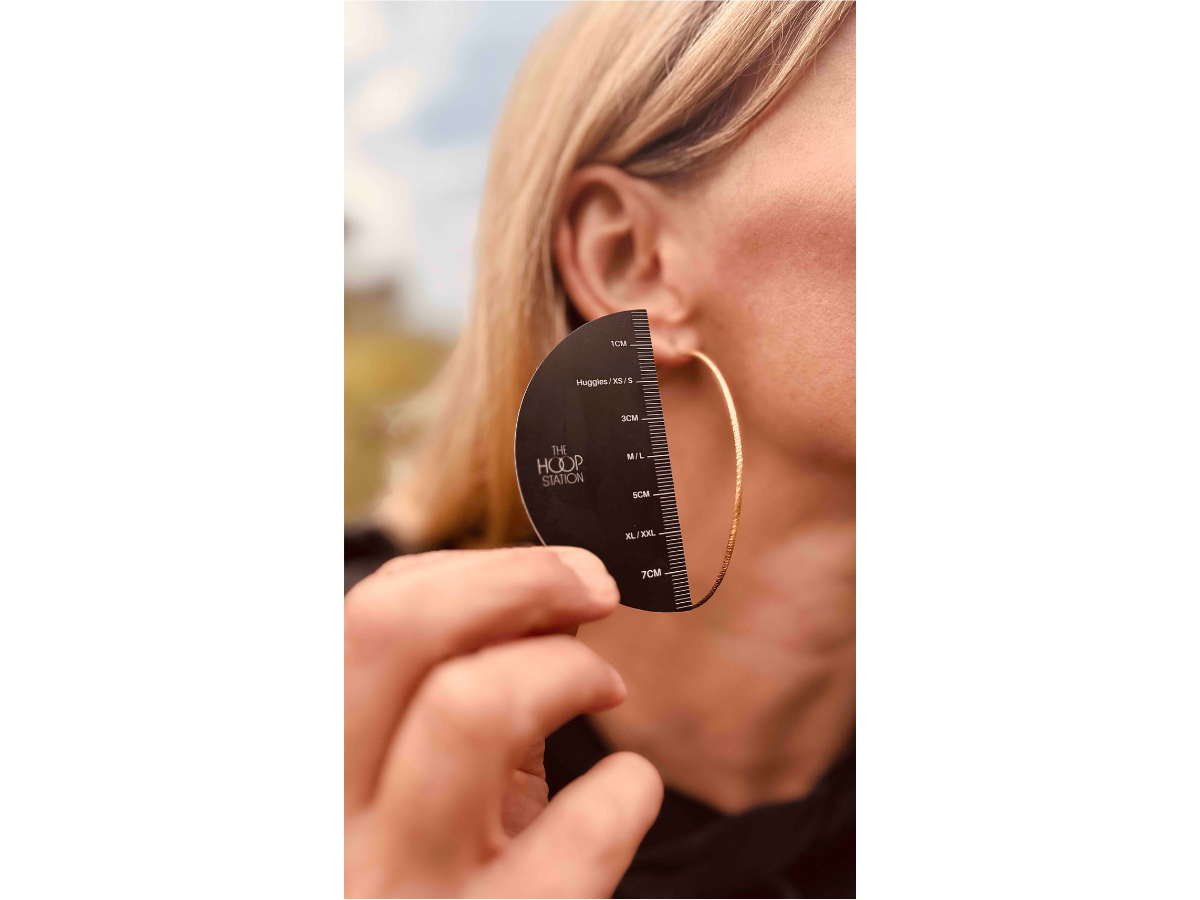 Person using a hoop earring size guide to measure an earring against their ear.