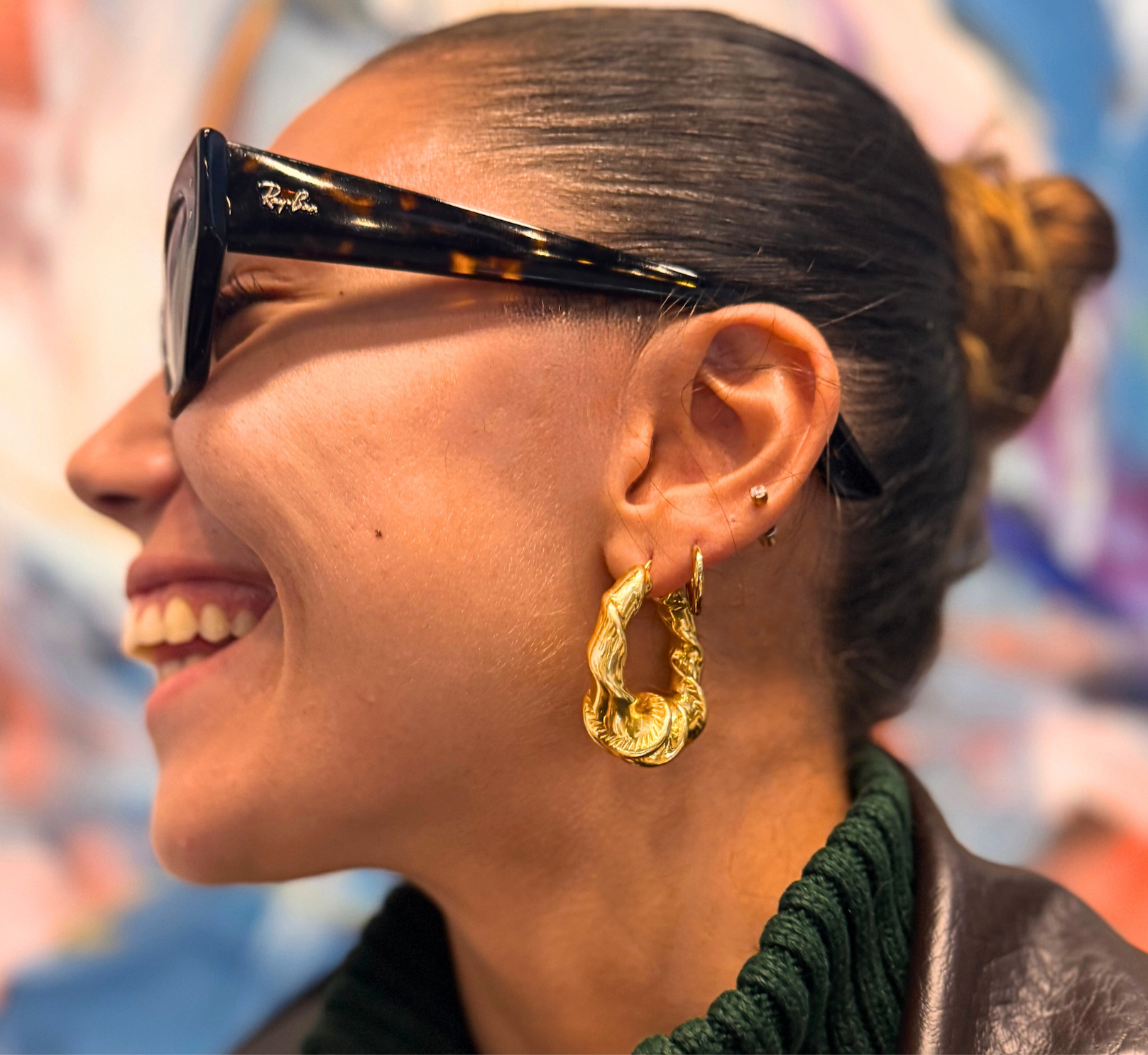 Woman wearing gold hoop earrings with a blurred colorful background