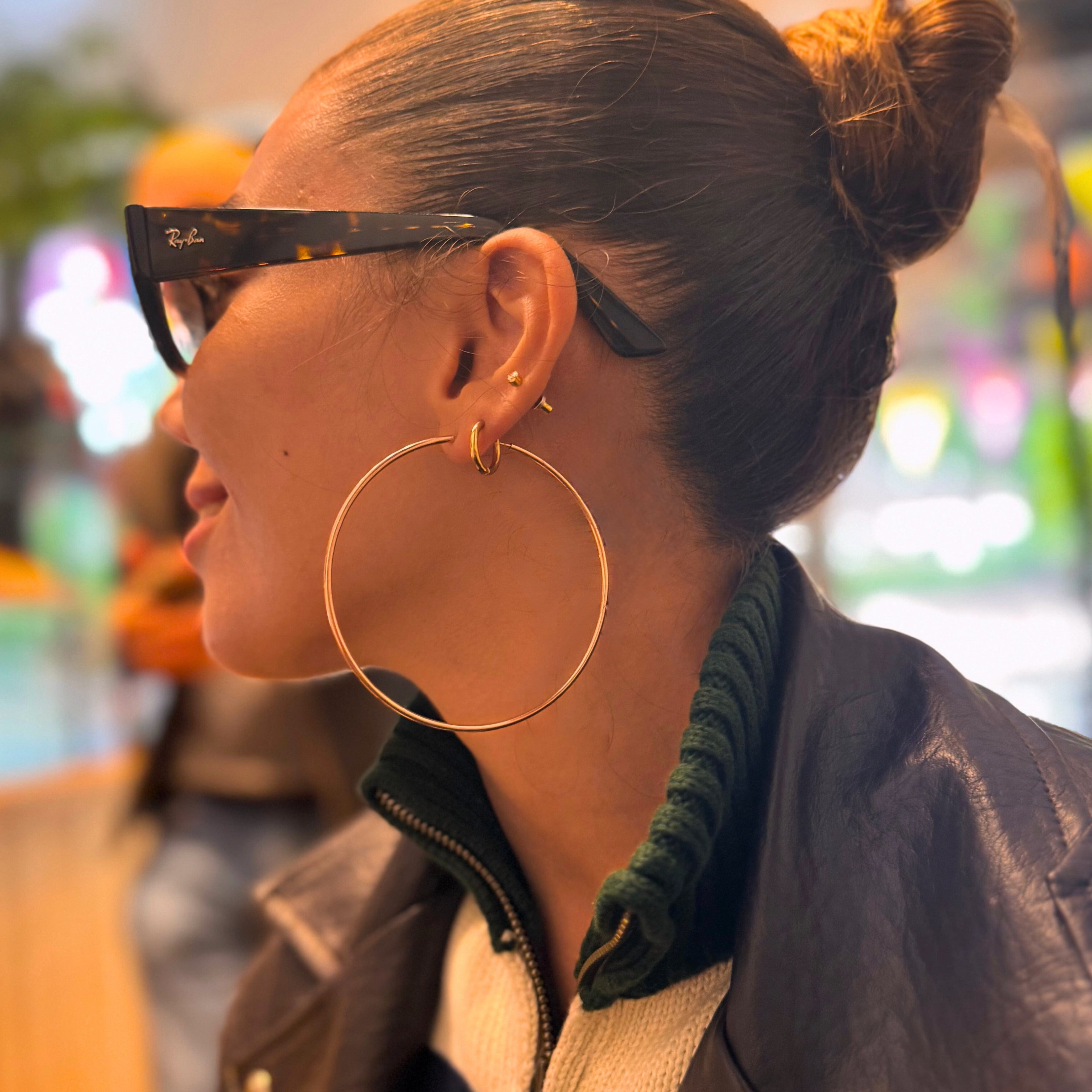 Person wearing large hoop earrings and a dark jacket with a blurred indoor background
