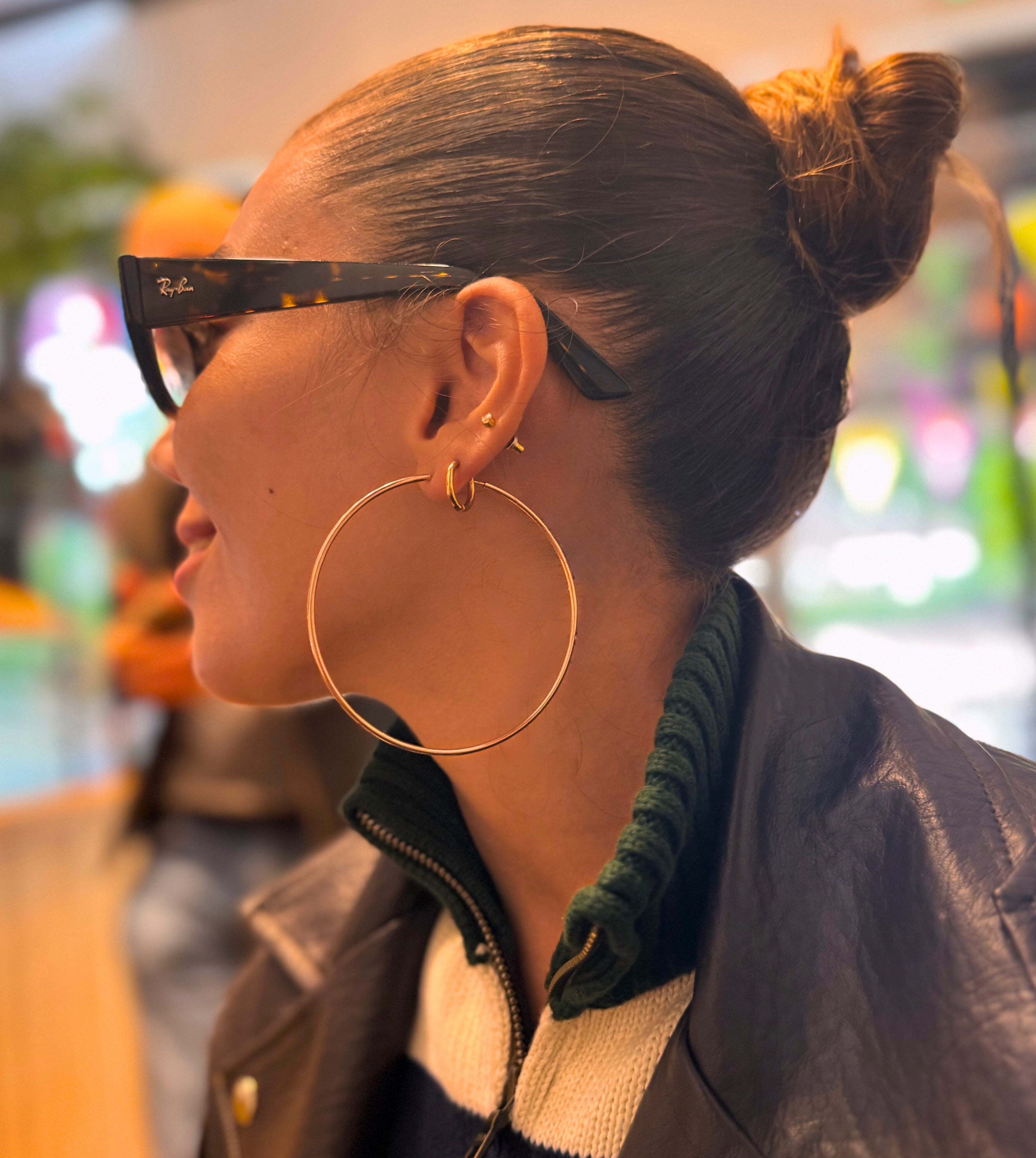 Person wearing large hoop earrings and a dark jacket with a blurred indoor background
