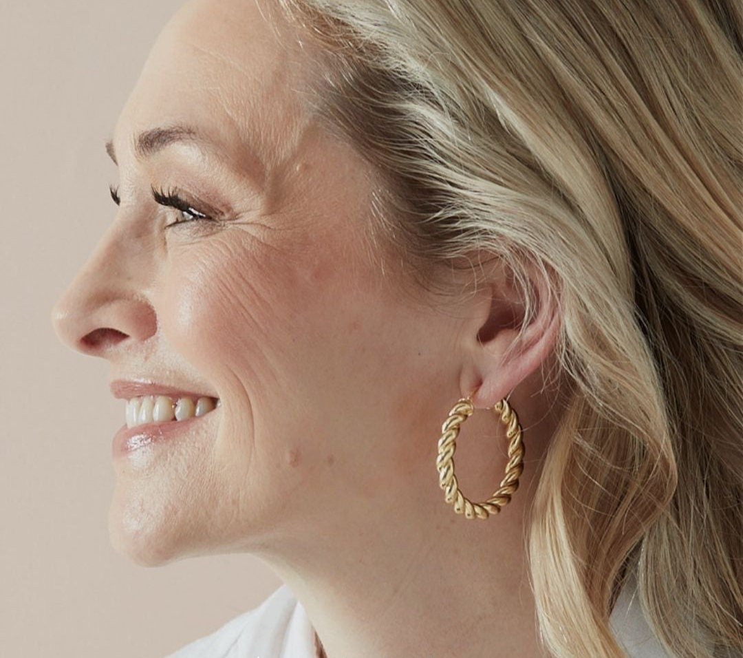 Woman wearing gold hoop earrings with a neutral background