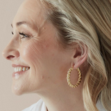 Woman wearing gold hoop earrings with a neutral background